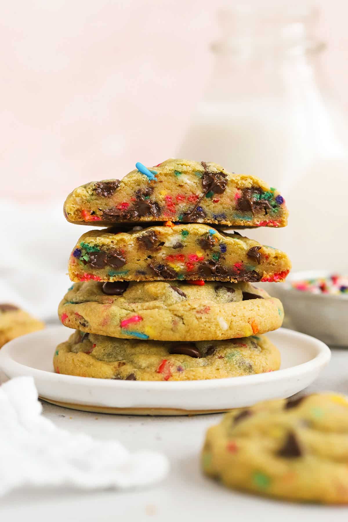 Three gluten-free chocolate chip cookies with sprinkles stacked on a white plate