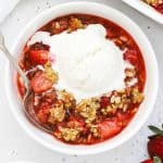 gluten free strawberry crisp in a white bowl topped with vanilla ice cream