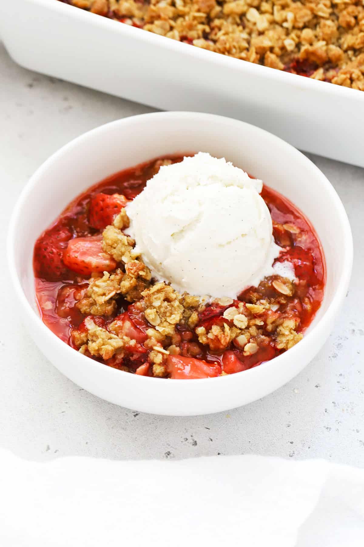 gluten free strawberry crisp in a white bowl topped with vanilla ice cream
