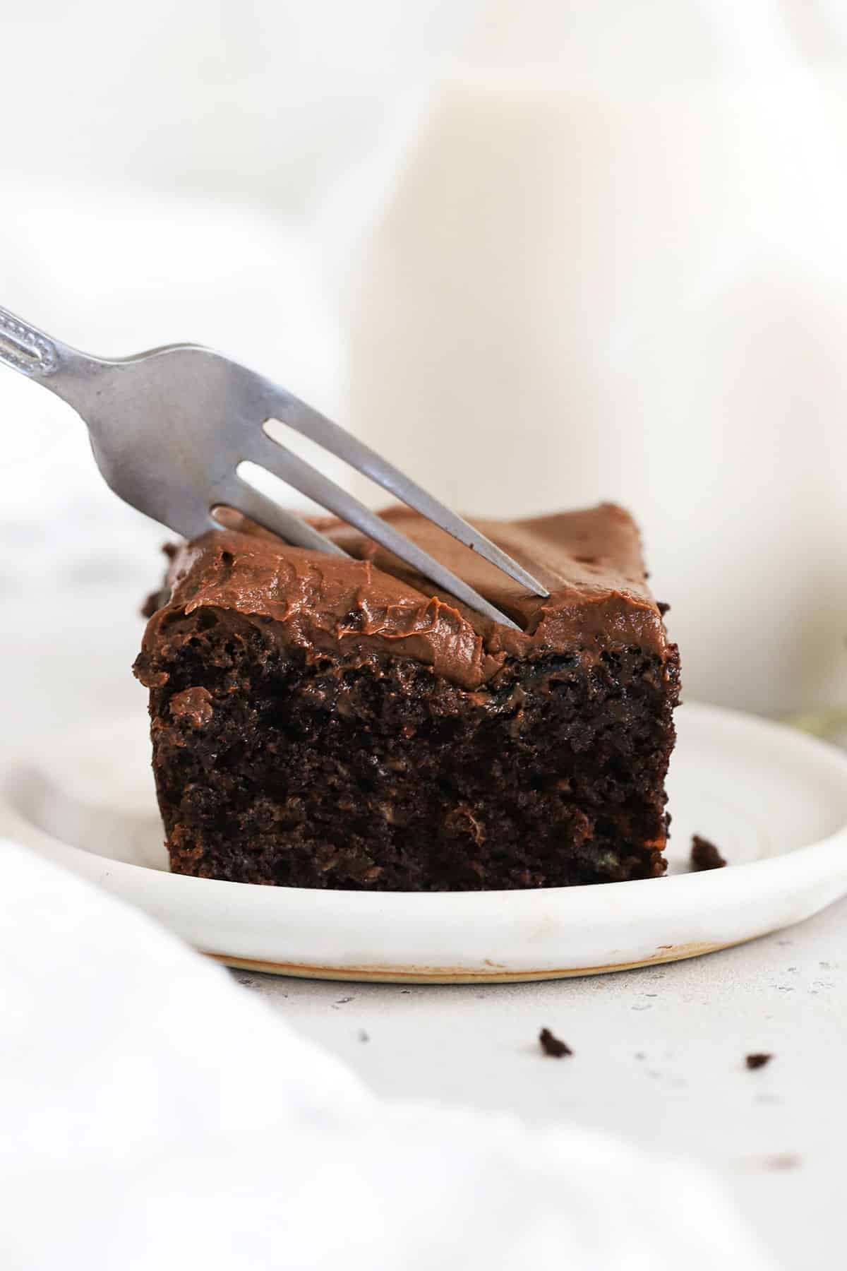 a fork cutting into a slice of gluten-free chocolate zucchini cake with chocolate frosting
