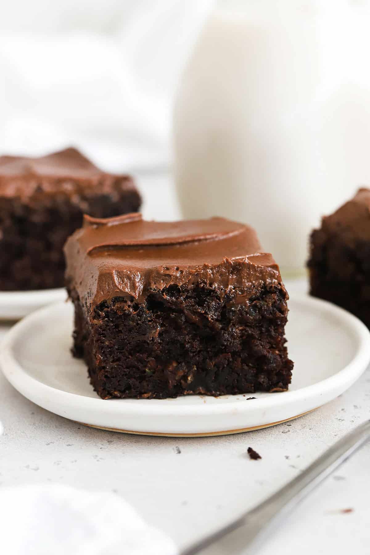 slices of gluten-free chocolate zucchini cake with chocolate frosting on white plates