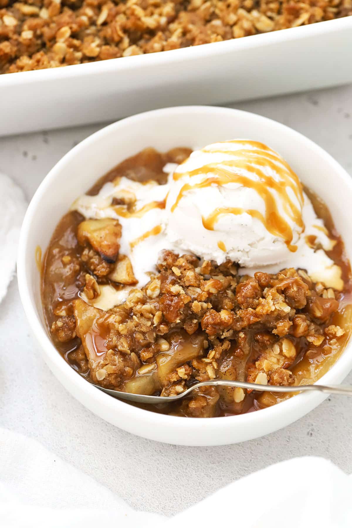 a bowl of gluten-free apple crisp with caramel sauce and a scoop of ice cream