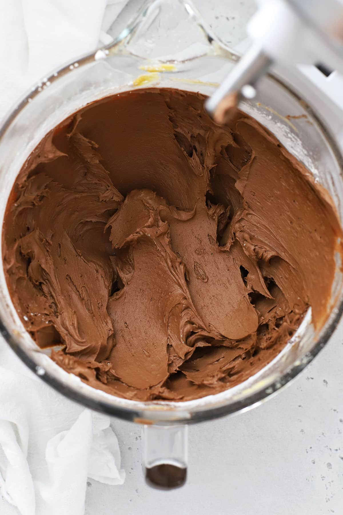 freshly mixed chocolate buttercream frosting in a glass mixing bowl