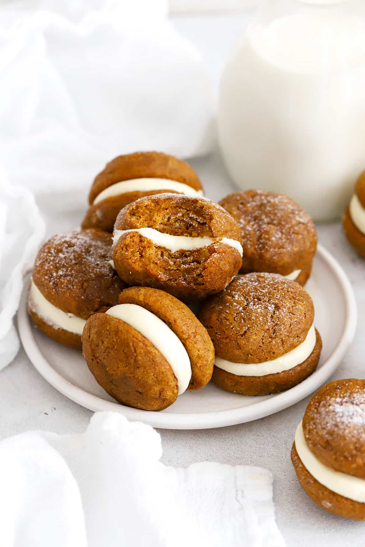 gluten-free pumpkin whoopie pies with cream cheese frosting stacked on a white plate