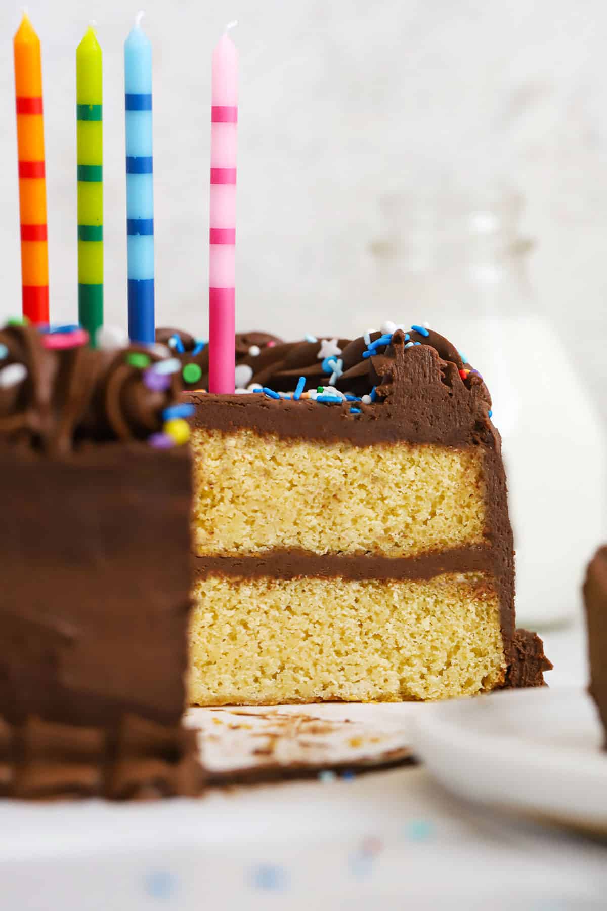 gluten-free yellow cake with chocolate frosting, colorful sprinkles, and colorful striped birthday candles