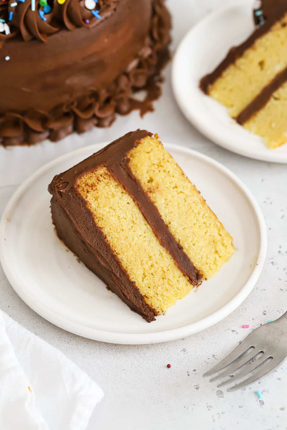 Slices of gluten-free yellow cake with chocolate frosting on white plates