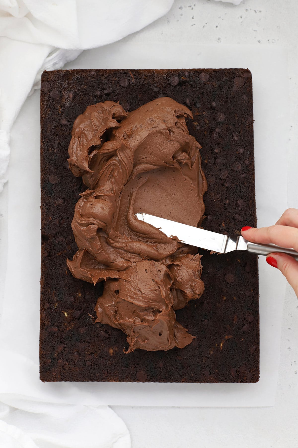 spreading chocolate buttercream frosting onto gluten-free chocolate zucchini cake