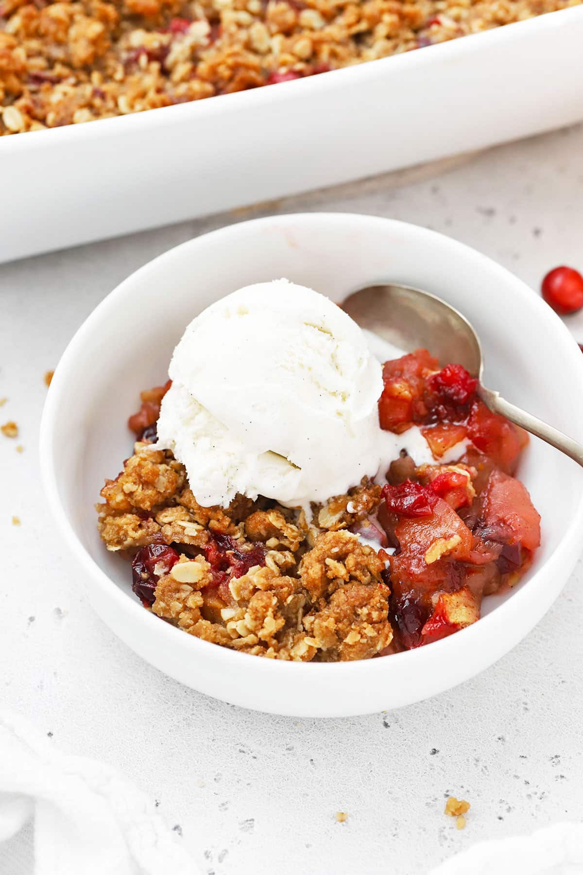 gluten-free apple cranberry crisp in a white bowl with a scoop of vanilla ice cream