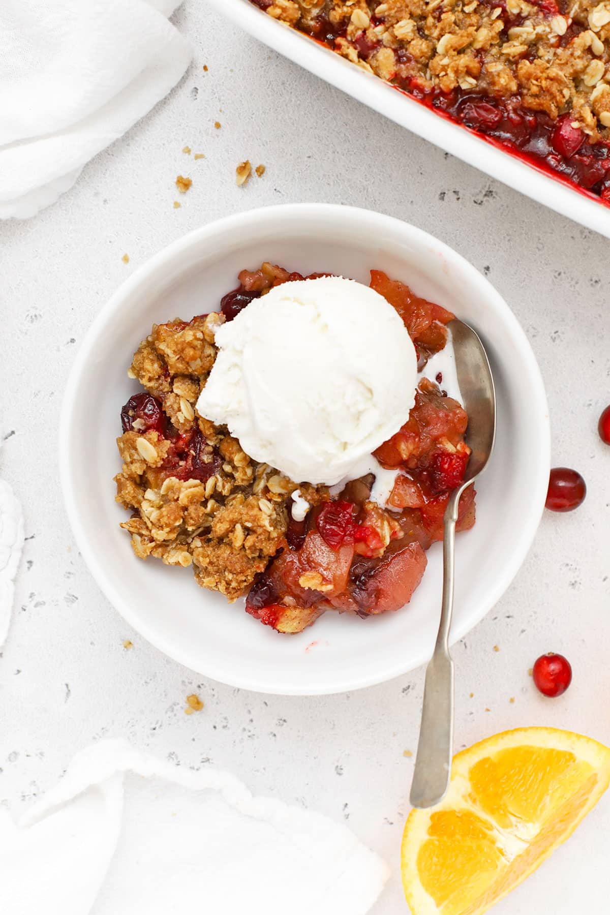 gluten-free apple cranberry crisp in a white bowl with a scoop of vanilla ice cream