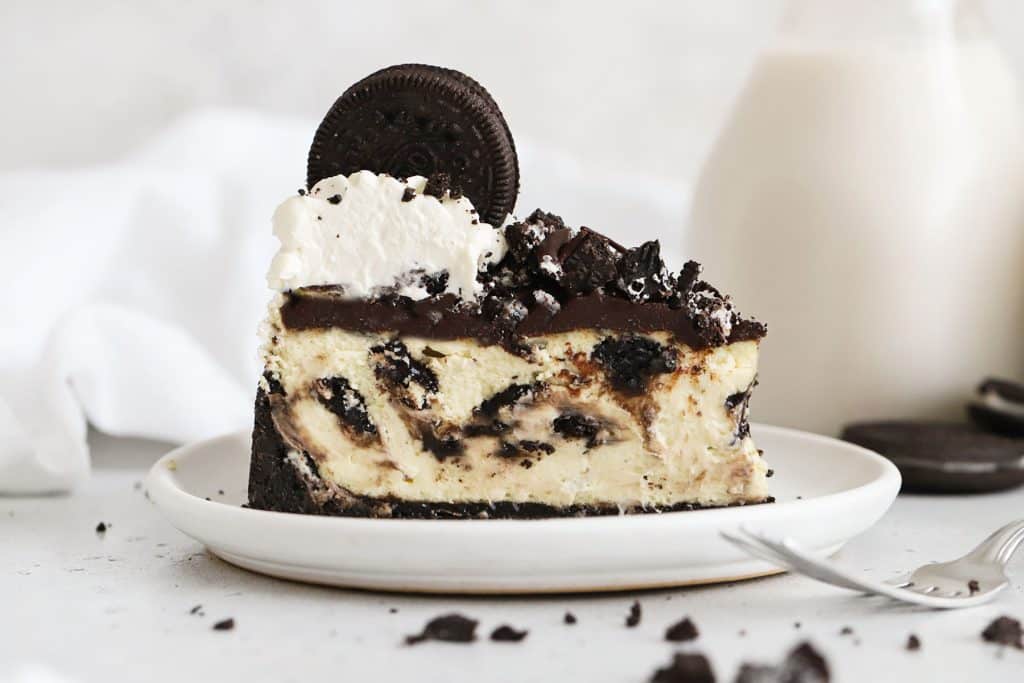 slice of gluten-free Oreo cheesecake topped with chocolate ganache, chopped Oreo cookies, and whipped cream