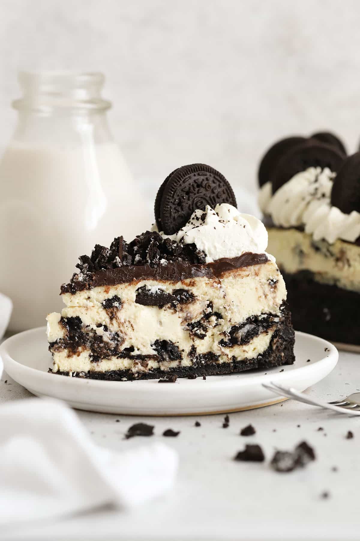 slice of gluten-free Oreo cheesecake topped with chocolate ganache, chopped Oreo cookies, and whipped cream