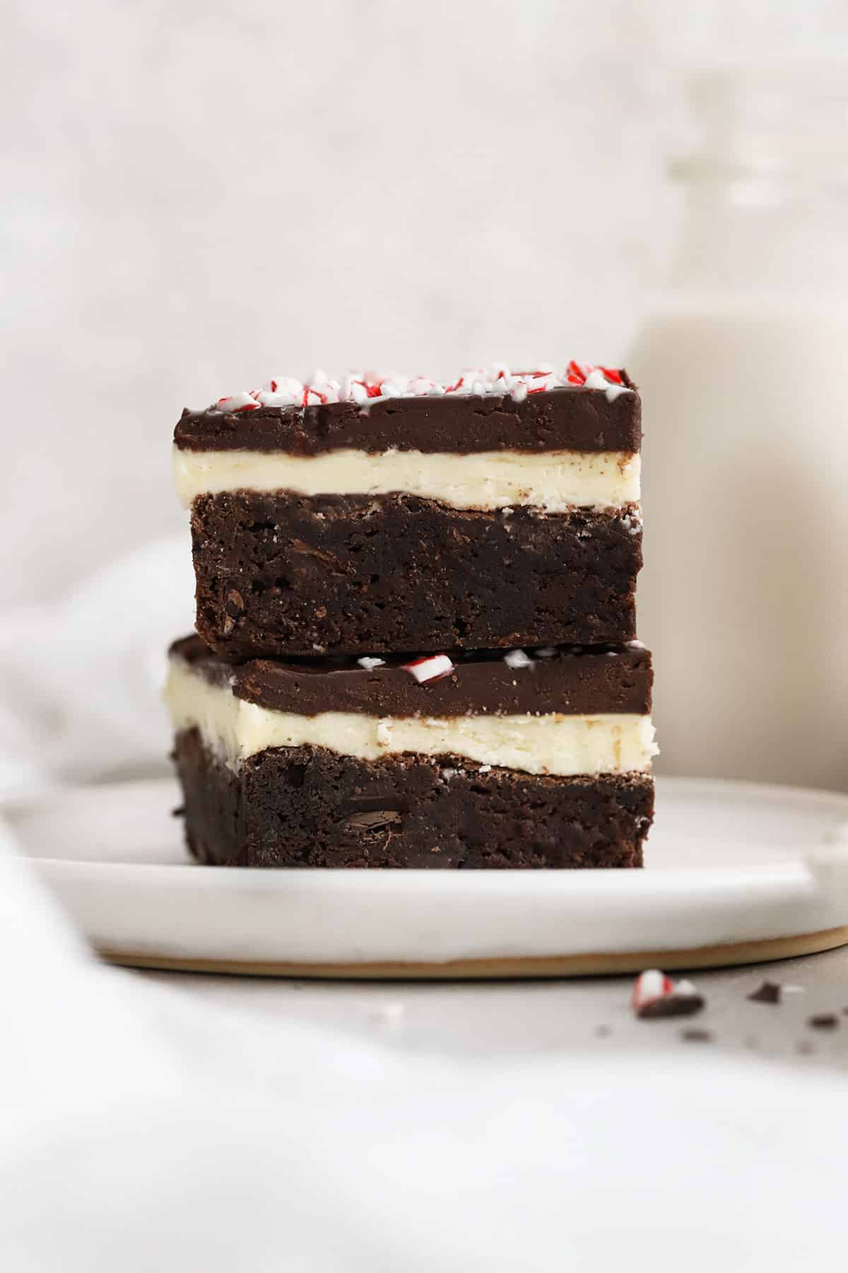 two gluten-free peppermint brownies with candy cane stacked on a white plate