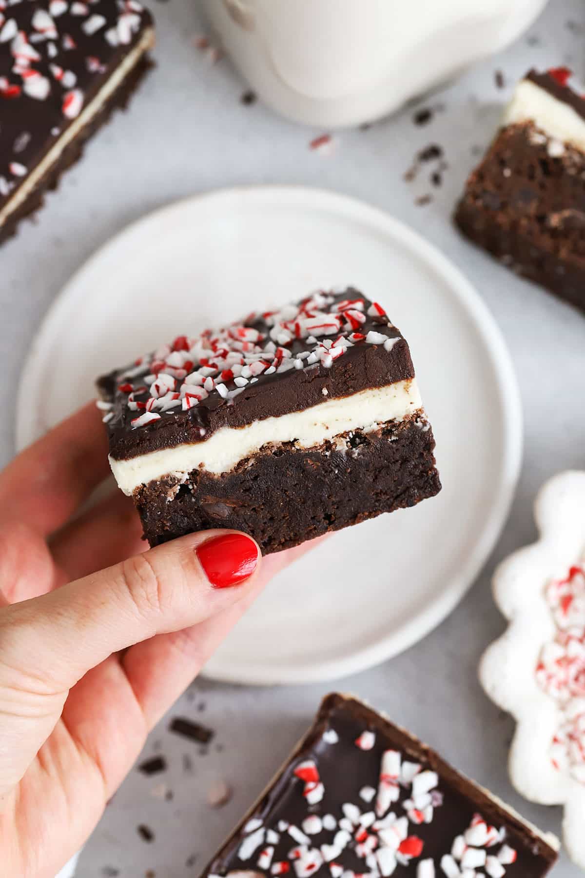hand holding a gluten-free peppermint brownie to show the 4 layers--brownie, peppermint cream cheese frosting, chocolate ganache, and crushed candy canes
