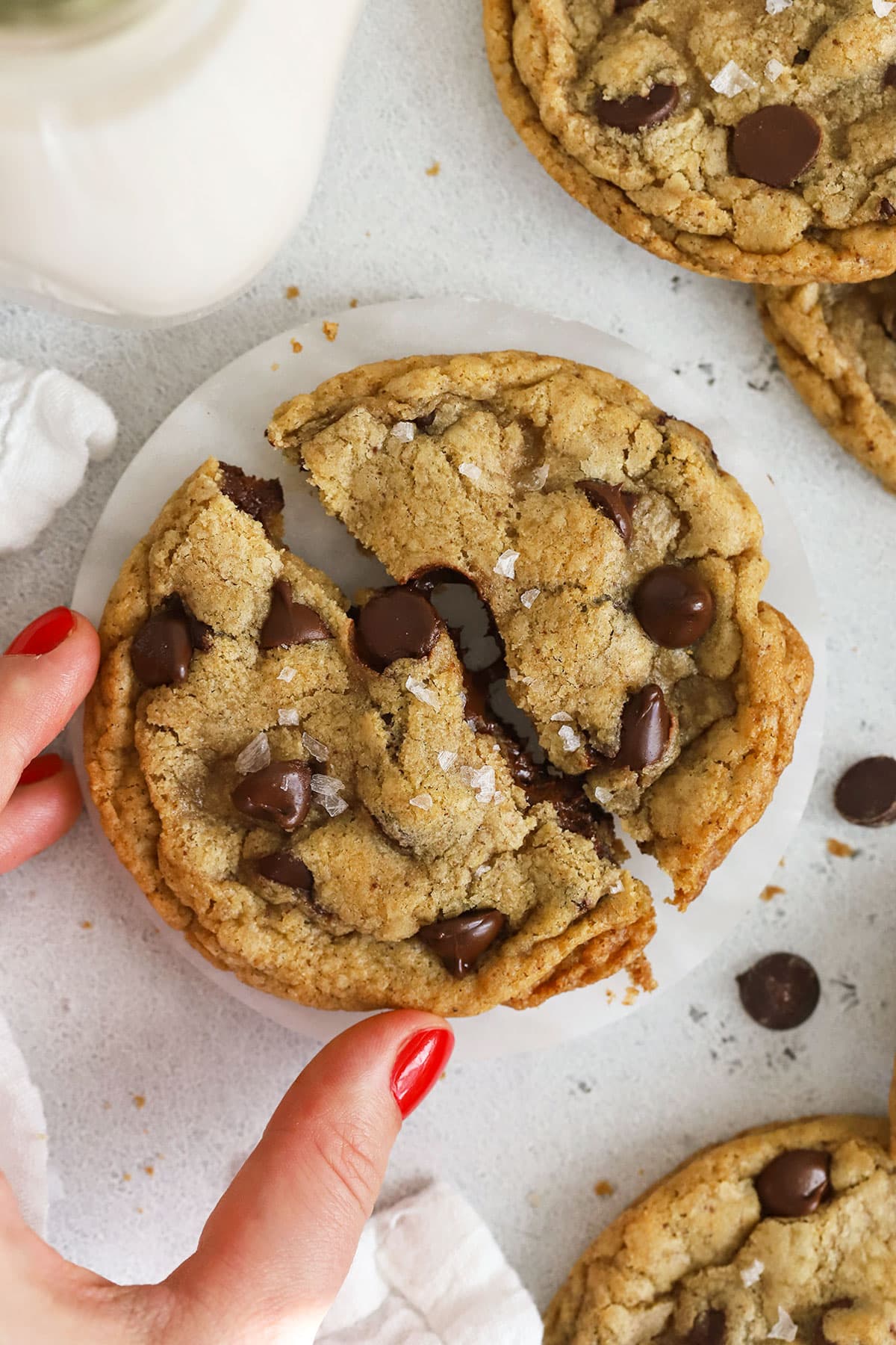 breaking a gluten-free brown butter chocolate chip cookie in half to show the gooey center