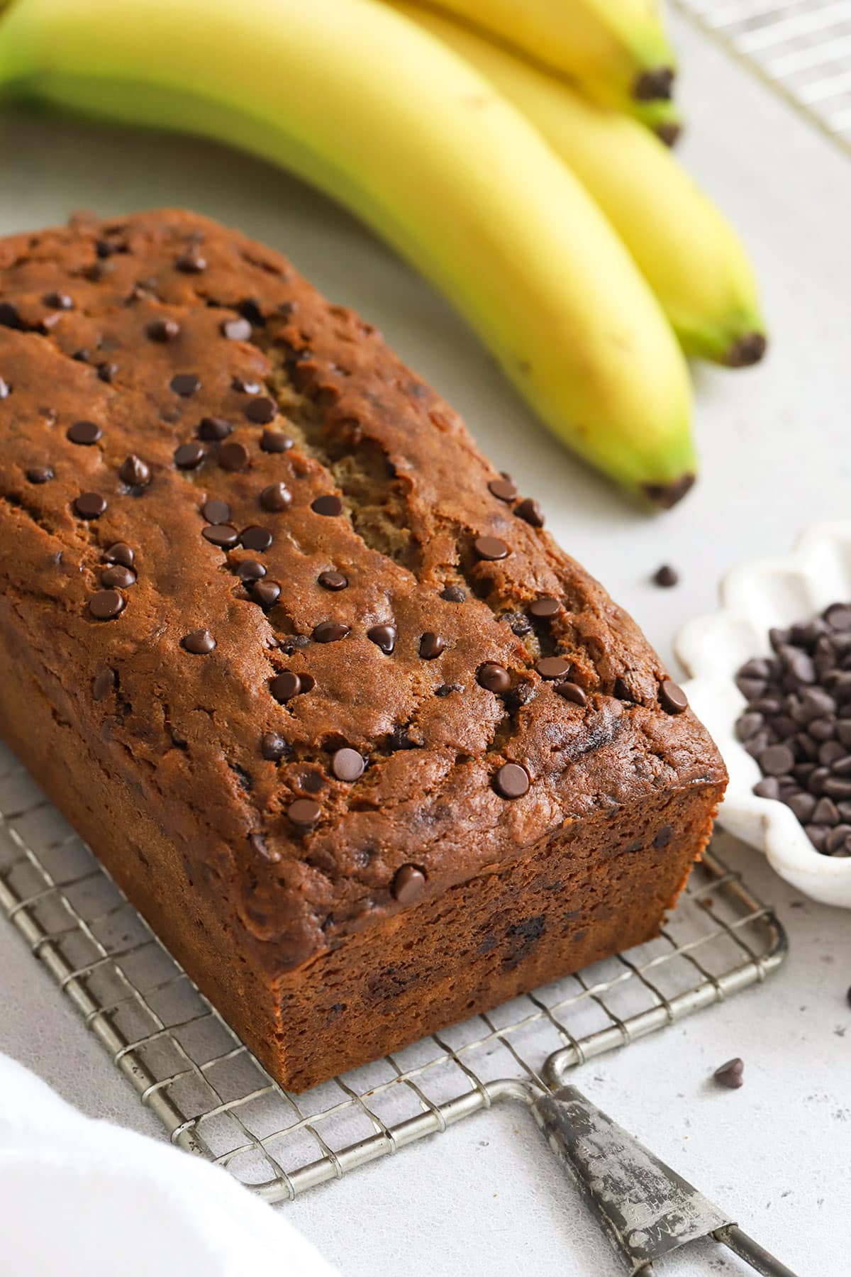 a loaf of gluten-free chocolate chip banana bread with chocolate chips and bananas in the background