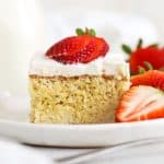 A slice of gluten-free tres leches cake topped with fresh strawberries on a white plate