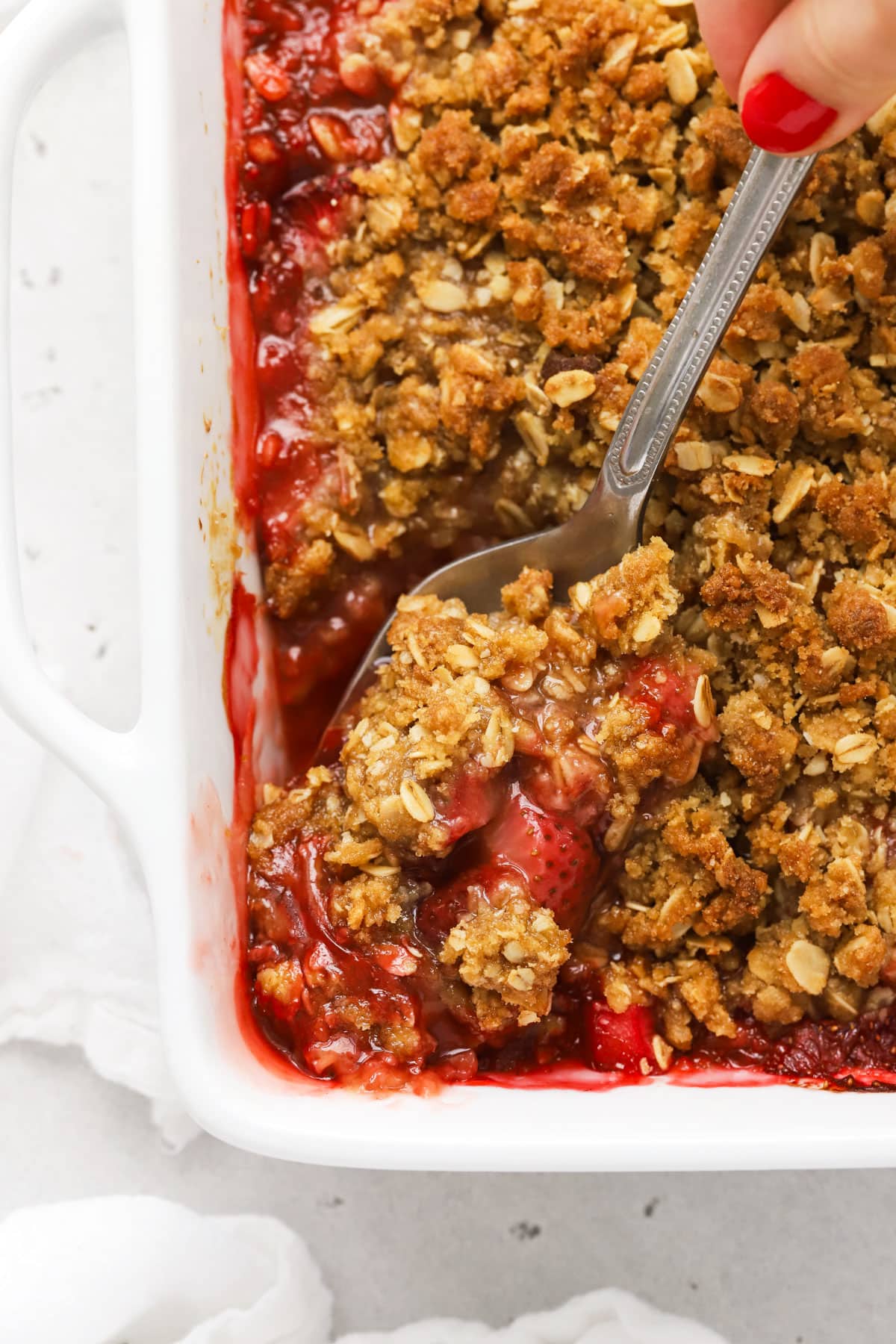 scooping a spoonful out of a pan of gluten free strawberry rhubarb crumble