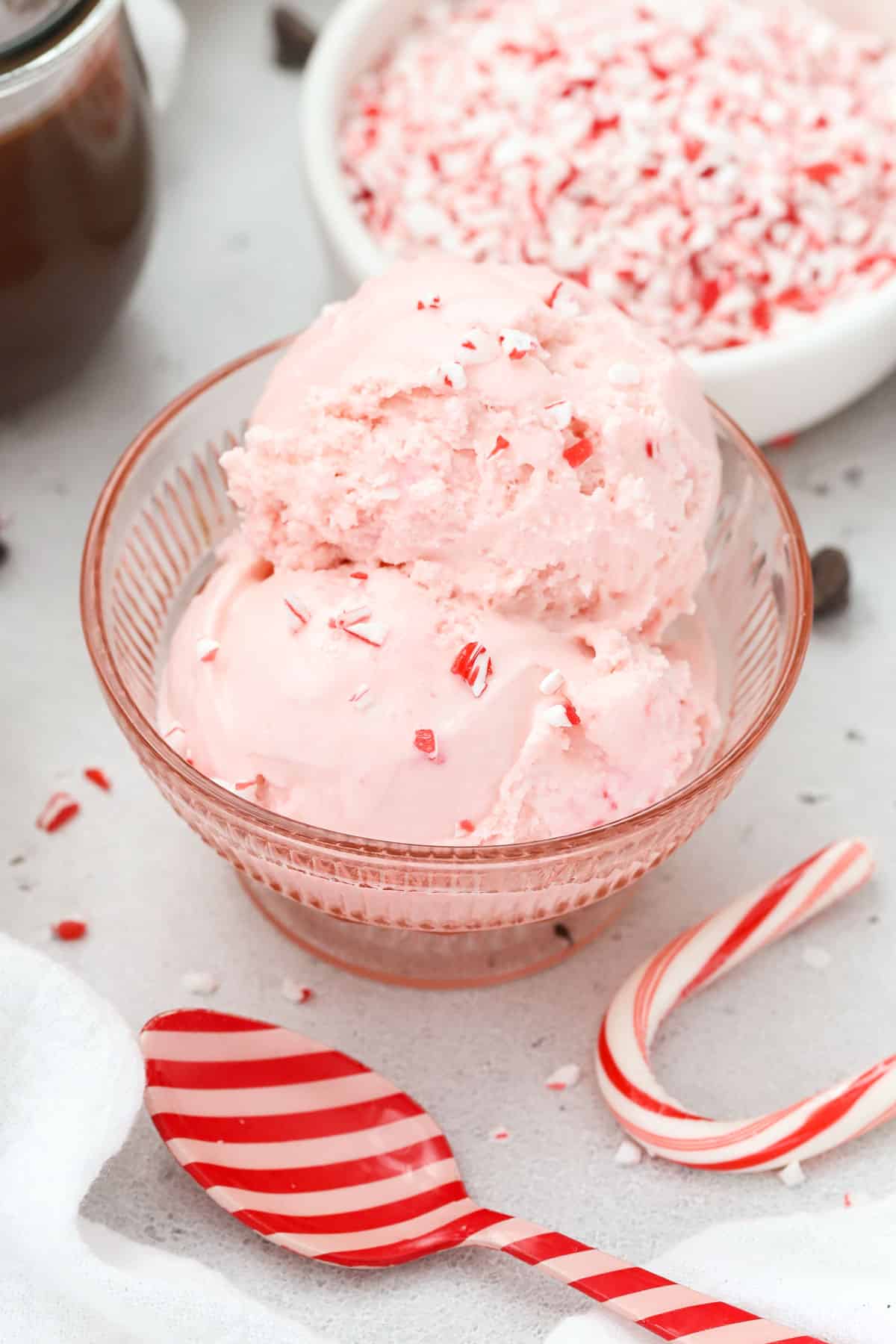 Scoops of Pink candy cane ice cream sprinkled with candy cane bits in a pink dessert bowl