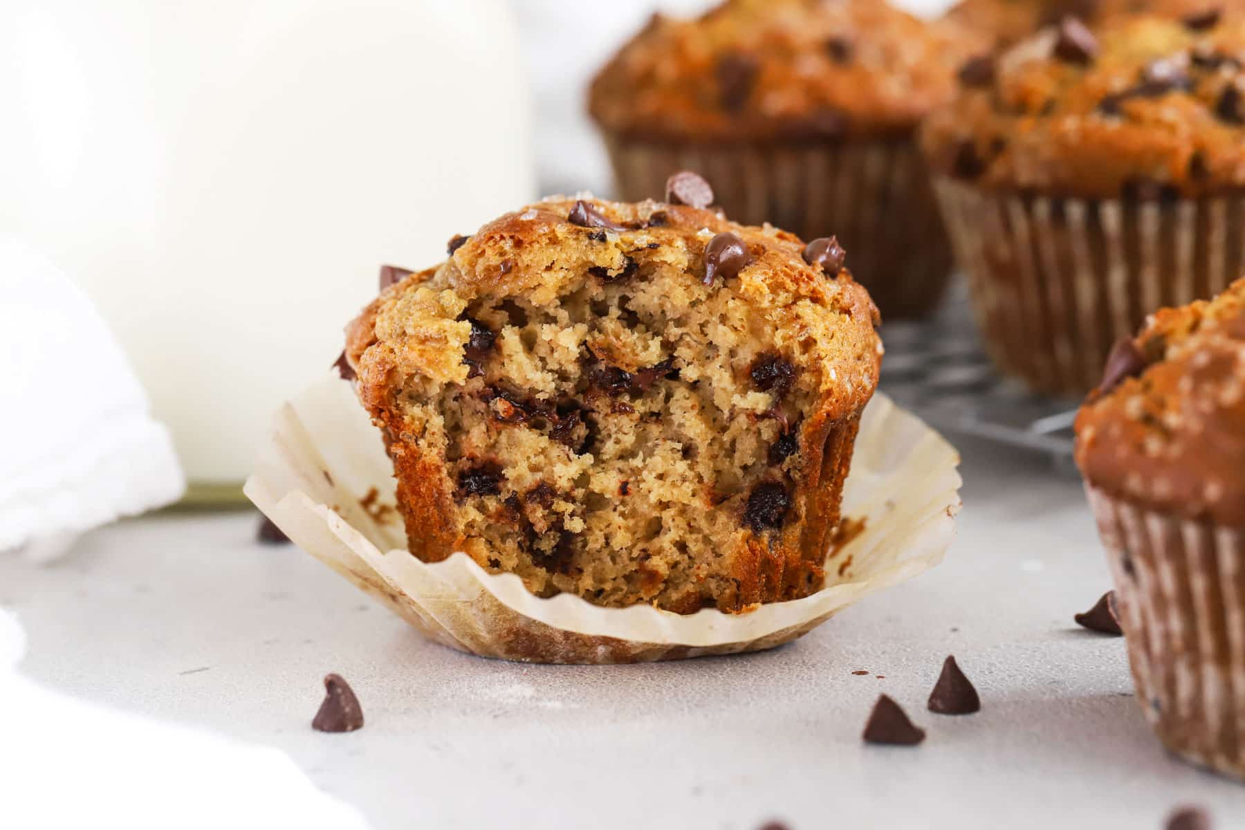 A gluten-free brown butter banana chocolate chip muffin with a bite out of it, showing the fluffy center