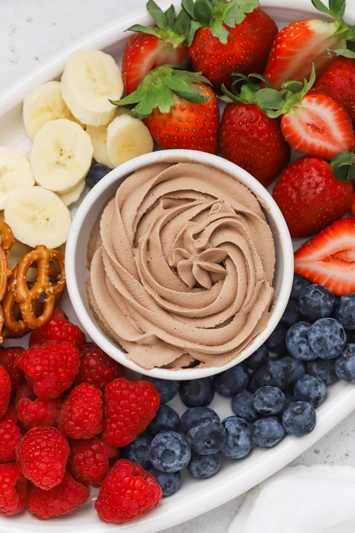 A bowl of chocolate whipped cream surrounded by colorful fresh fruit
