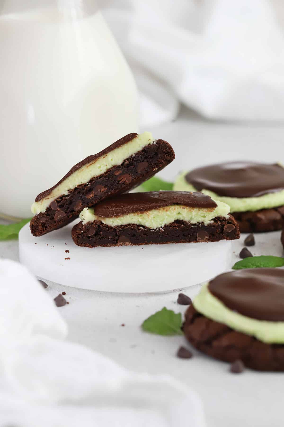 Gluten-free mint brownie cookies with ganache, cut in half and stacked next to a bottle of milk
