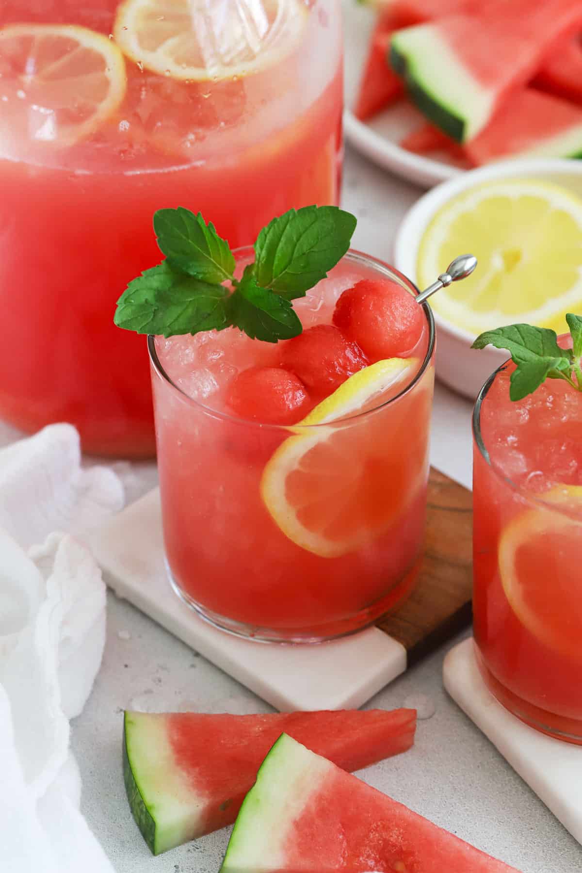 a glass of watermelon lemonade garnished with watermelon balls, fresh mint, and lemon slices