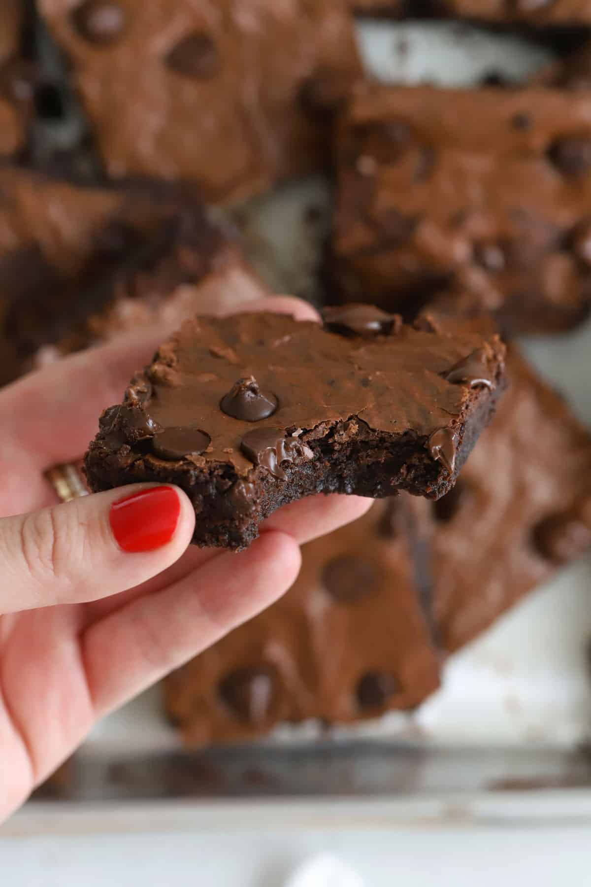Hand holding a fudgy gluten-free sheet pan brownie with a bite taken out of it